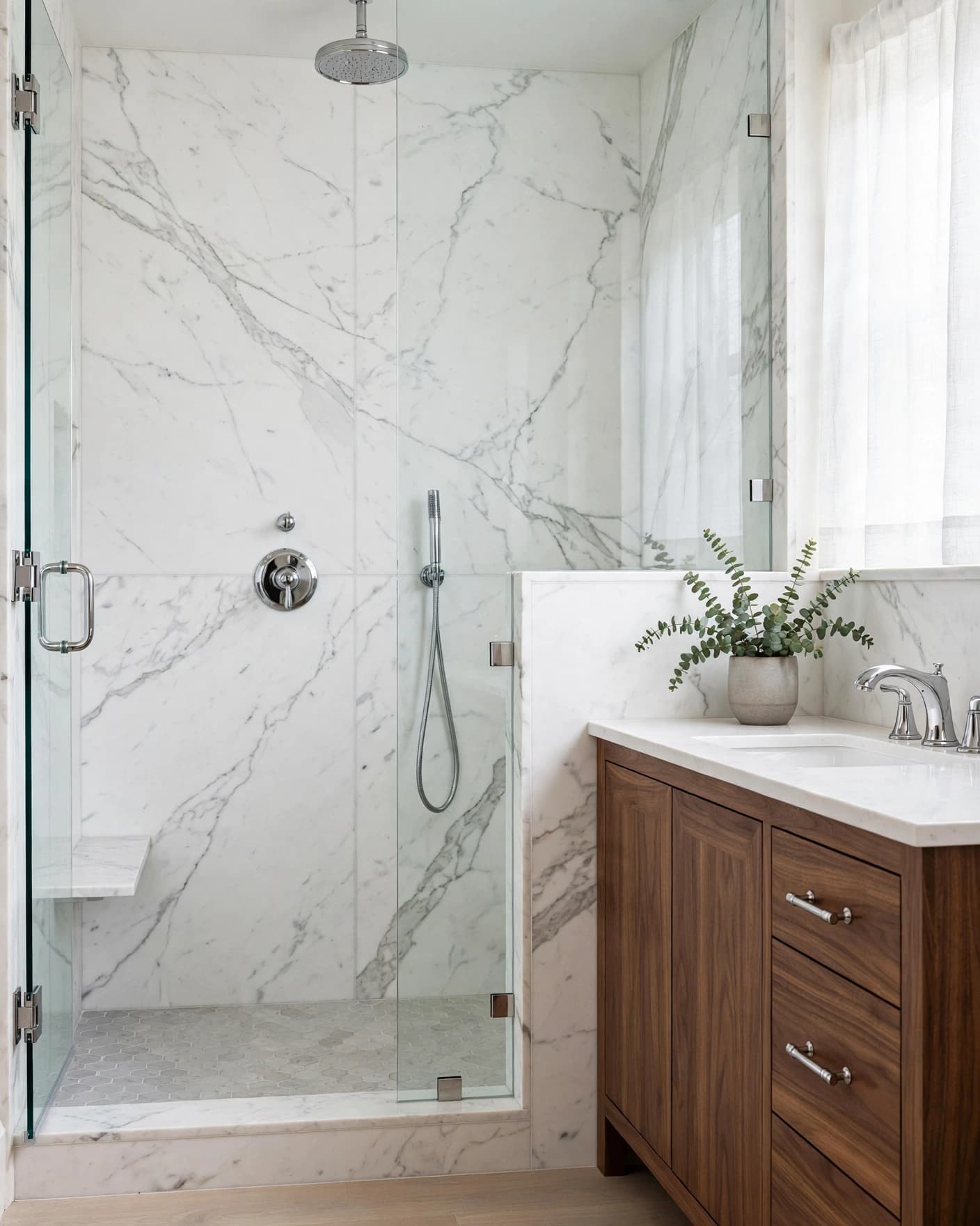 White marble shower wall beside a walnut vanity with chrome fixtures and glass doors.