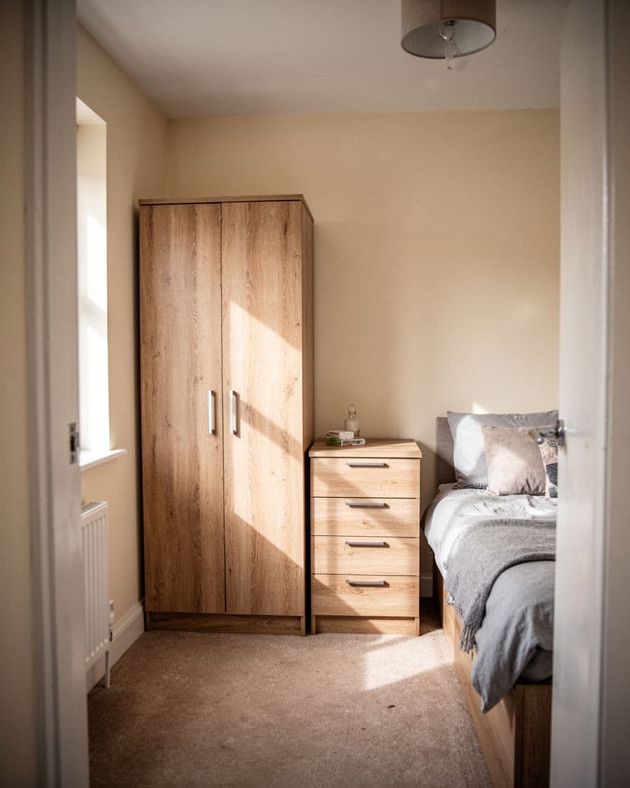 A light wood wardrobe and narrow dresser in a small cream-walled bedroom.