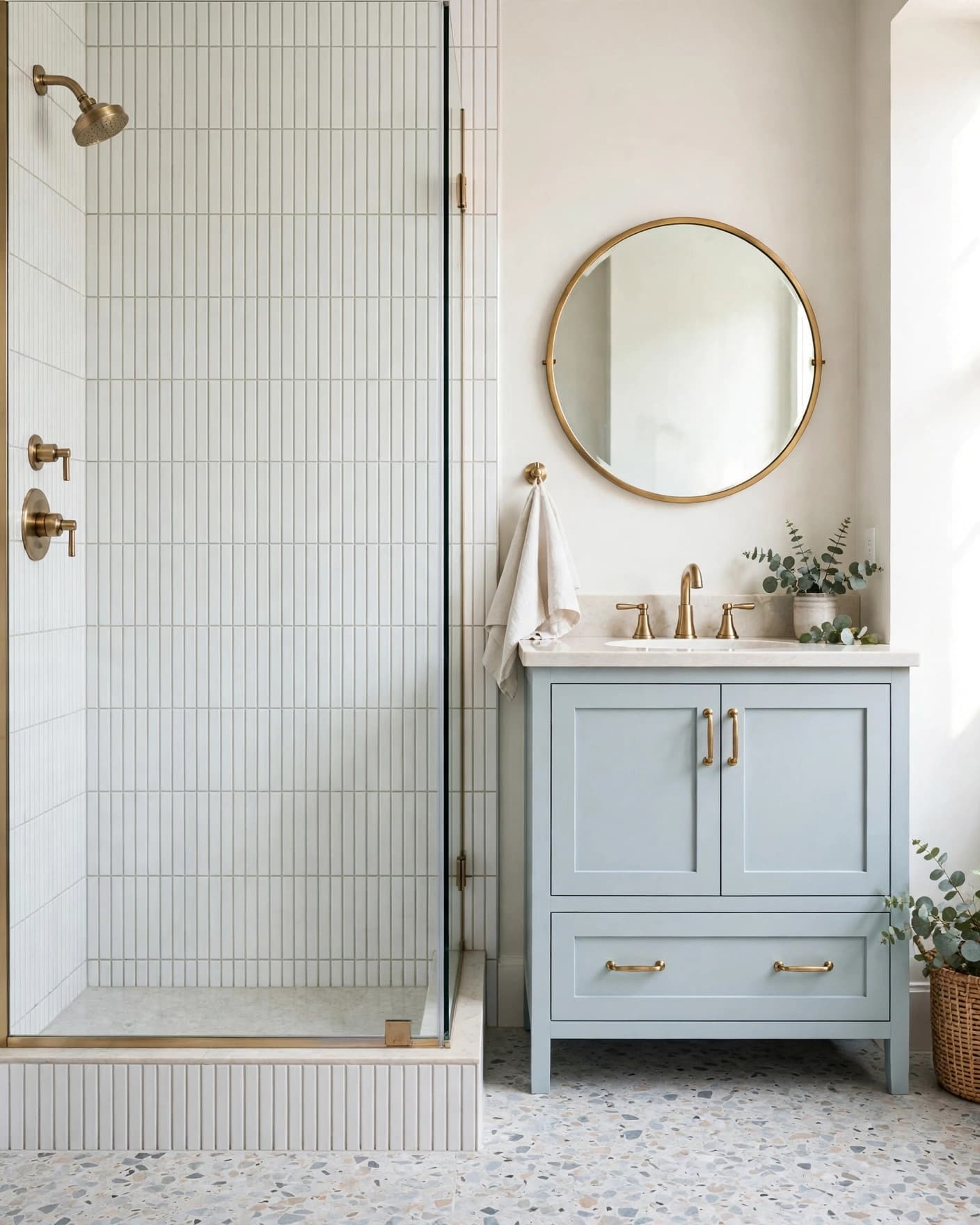 Bright bathroom with vertical white shower tile, blue vanity, brass fixtures, and a round mirror.