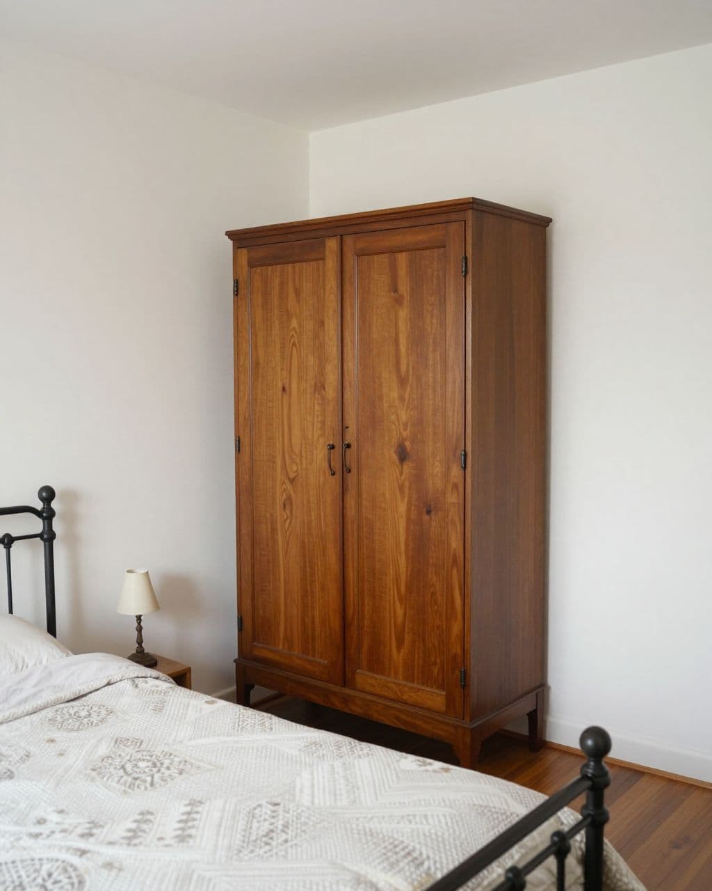 A walnut armoire stands beside an iron bed in a small bedroom.